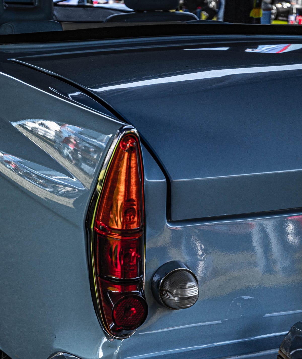 Rear quarter of an older car in blue-grey, reflections running unbroken along the panel